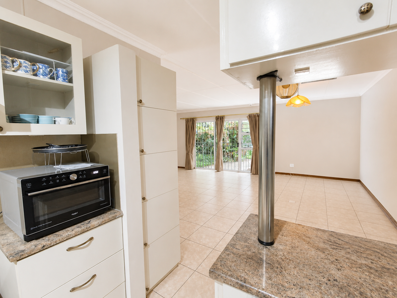 Open-plan kitchen and living area featuring neutral cabinetry, granite countertops, tiled flooring, and sliding doors leading to the exterior.