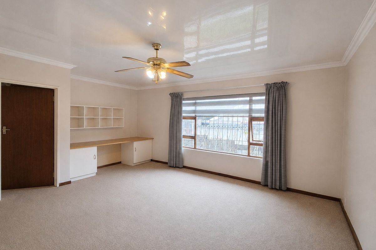 Spacious bedroom featuring a built-in desk and shelving unit, carpeted flooring, a ceiling fan, and large windows with security bars.