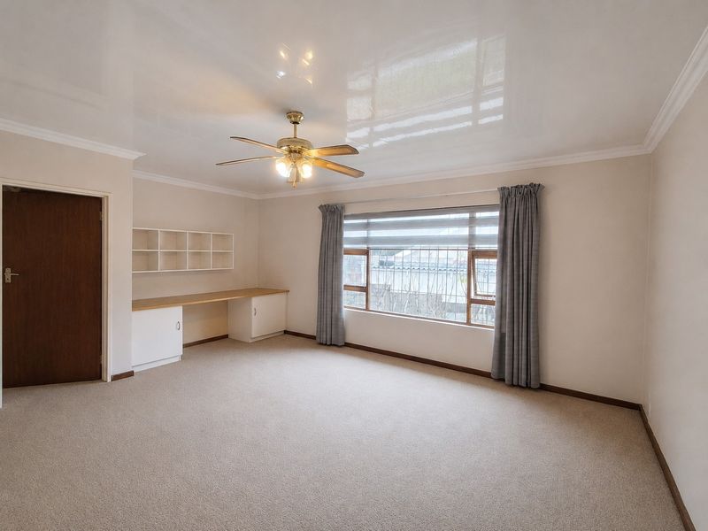 Spacious bedroom featuring a built-in desk and shelving unit, carpeted flooring, a ceiling fan, and large windows with security bars.