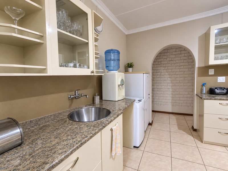 A functional scullery featuring granite countertops, stainless steel sink, built-in cabinetry, and a distinctive brick archway leading to an adjacent space.