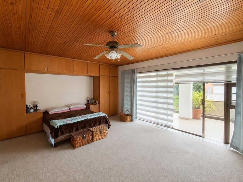 Spacious bedroom featuring extensive built-in cabinetry, a warm timber-clad ceiling, ceiling fan, and large sliding doors providing direct access to an outdoor patio area.