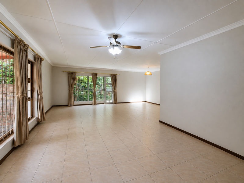 Spacious, light-filled living area featuring neutral tiled flooring, a ceiling fan, and large sliding glass doors providing access to the garden.
