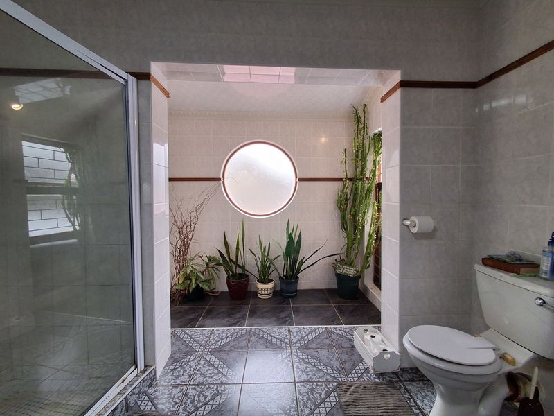 A bathroom featuring a shower enclosure, toilet, and a distinctive circular porthole window with tiled finishes throughout.