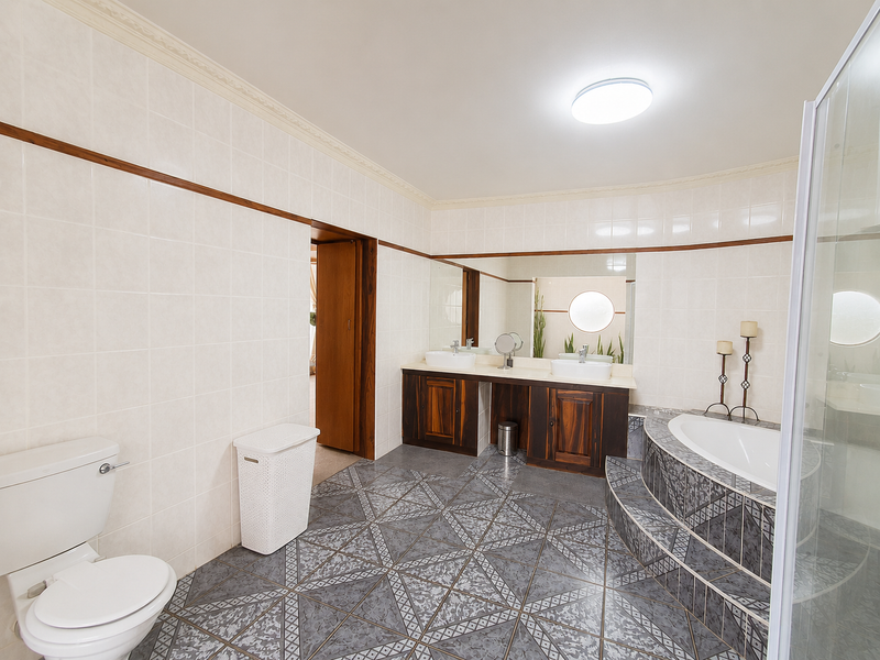 Spacious bathroom featuring a double vanity with vessel sinks, a raised platform bathtub, a separate shower enclosure, and decorative ceramic floor tiling.