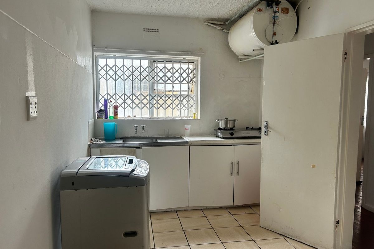 A compact kitchen featuring basic cabinetry, a stainless steel sink, tiled flooring, and an integrated electric water heater.