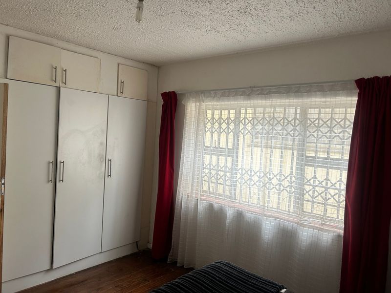 Bedroom featuring built-in cupboards, hardwood flooring, and a window with security gate. The room requires cosmetic updates to the ceiling and cabinetry.