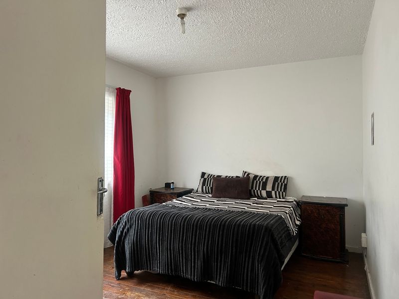 A bedroom featuring hardwood flooring and a textured ceiling, currently requiring cosmetic updates to improve its overall condition and appeal.