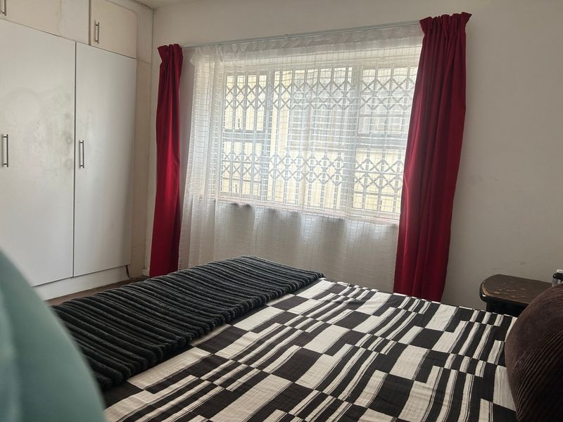 A bedroom featuring built-in cupboards and a window fitted with a security gate.