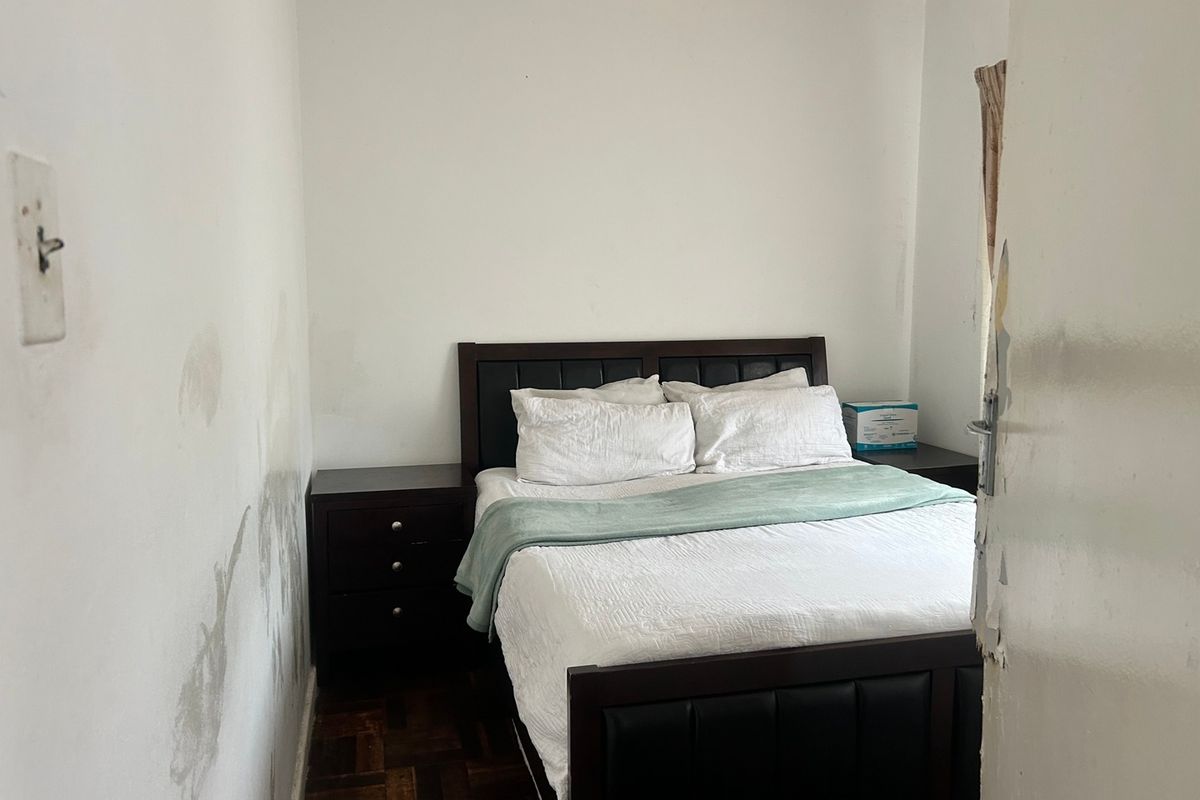 A compact bedroom featuring parquet flooring, currently showing significant wall surface damage and wear on the door frame.