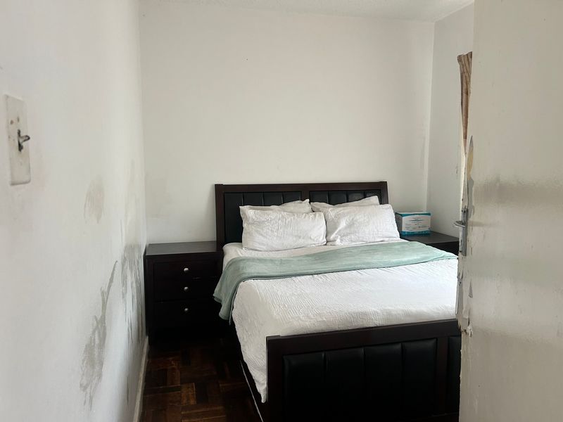 A compact bedroom featuring parquet flooring, currently showing significant wall surface damage and wear on the door frame.