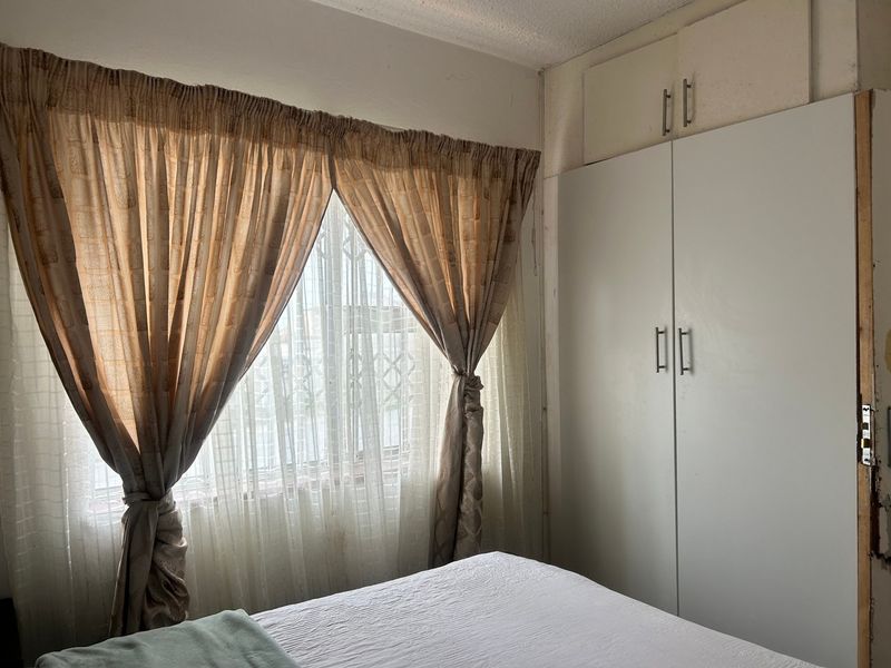 A bedroom featuring a built-in wardrobe with overhead storage cupboards and a window fitted with a security gate.