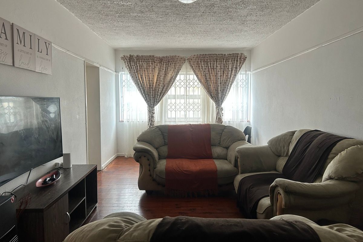 A living room featuring hardwood flooring, a textured ceiling, and a window with security bars, offering a functional and comfortable living space.