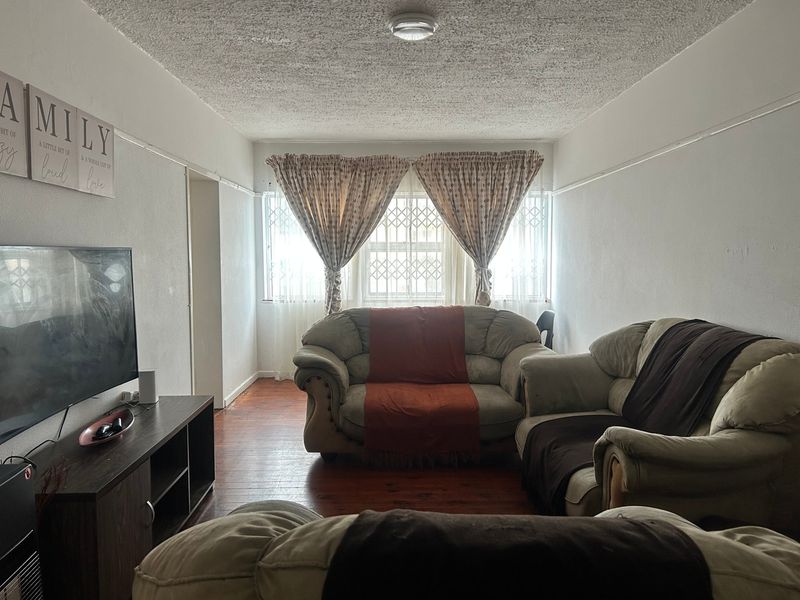 A living room featuring hardwood flooring, a textured ceiling, and a window with security bars, offering a functional and comfortable living space.