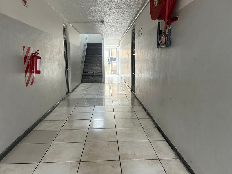 A functional apartment building hallway featuring tiled flooring, a staircase, and essential fire safety equipment including a hose reel and extinguisher.