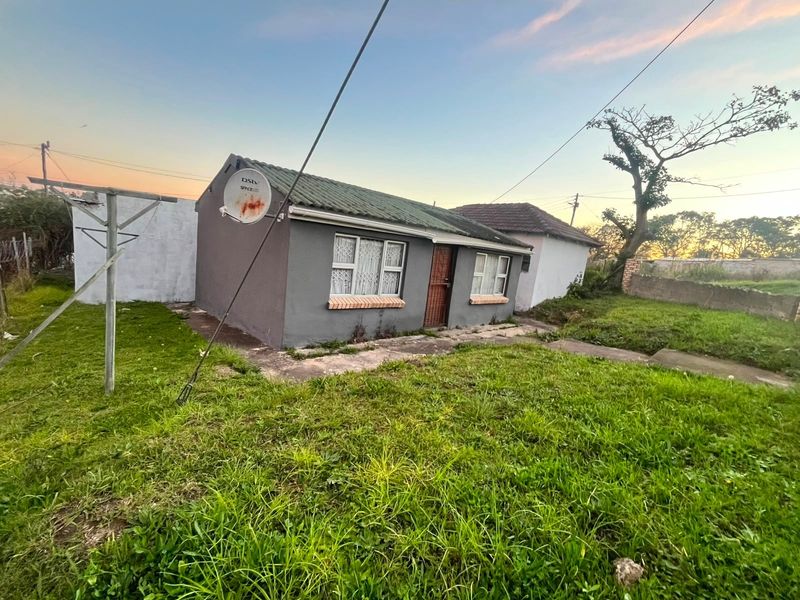 Front exterior view of a modest single-story house featuring a tiled roof, security gate, and surrounding garden area with a concrete pathway.