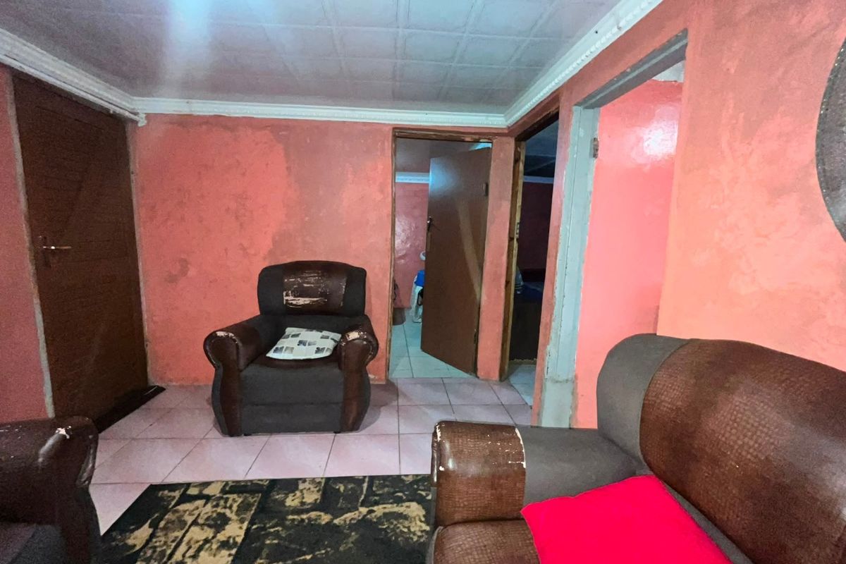 A living room area featuring tiled flooring and ceiling tiles, currently requiring cosmetic updates to the wall finishes and general maintenance.