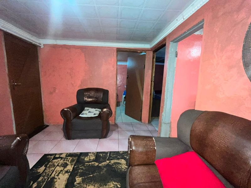 A living room area featuring tiled flooring and ceiling tiles, currently requiring cosmetic updates to the wall finishes and general maintenance.