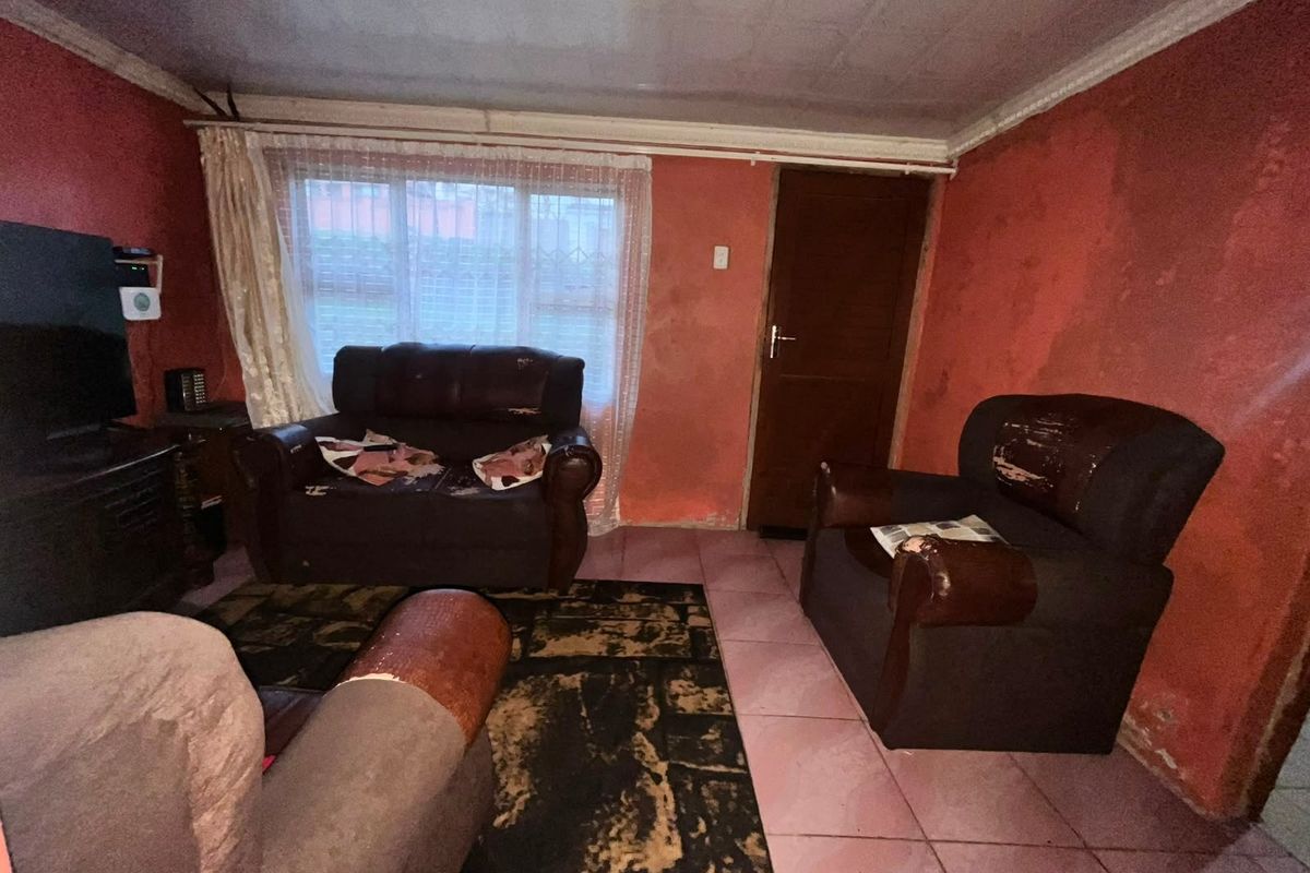 A living room featuring tiled flooring and a timber door, currently requiring significant cosmetic updates to the wall finishes and overall interior presentation.