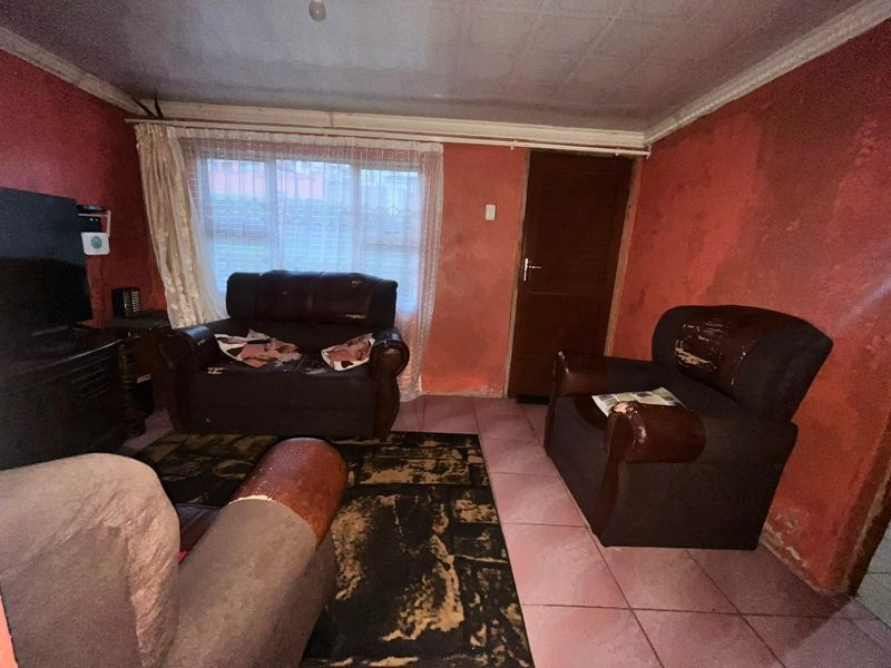 A living room featuring tiled flooring and a timber door, currently requiring significant cosmetic updates to the wall finishes and overall interior presentation.