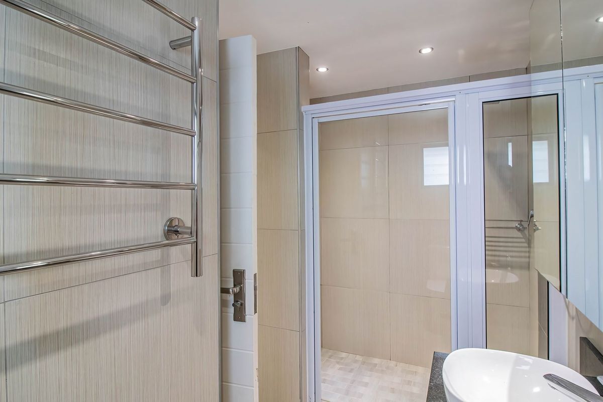 Modern bathroom featuring a glass shower enclosure, vanity basin, and a chrome heated towel rail with neutral wall and floor tiling.