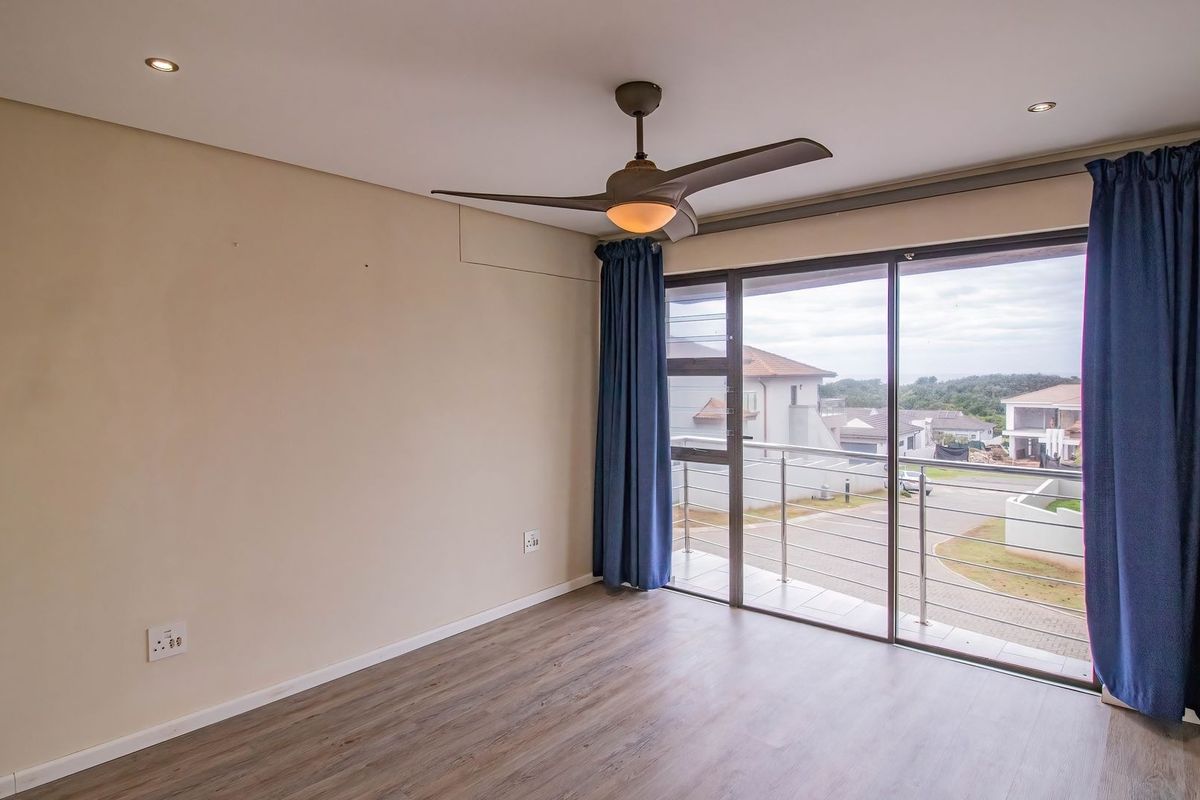 A bright, empty bedroom featuring laminate flooring, a ceiling fan, and a sliding glass door that opens onto a private balcony.