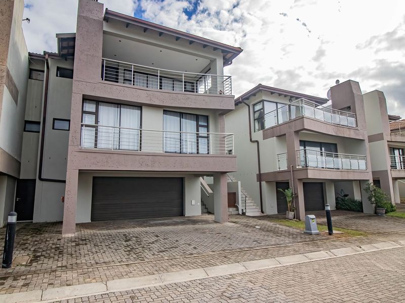 Front elevation of a multi-story townhouse complex featuring paved driveways, integrated garages, and private balconies with stainless steel railings.
