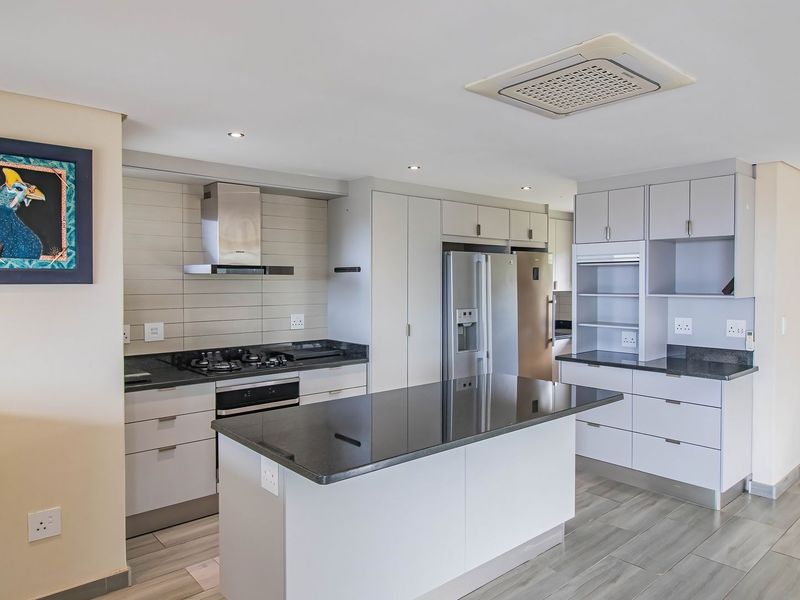 Modern kitchen featuring a central island, granite countertops, gas hob, extractor fan, and ample built-in cabinetry with integrated appliances.