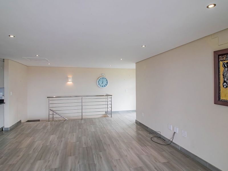 An open-plan living area featuring modern tiled flooring, recessed lighting, and a sleek stainless steel balustrade overlooking the staircase, adjacent to a compact kitchen.