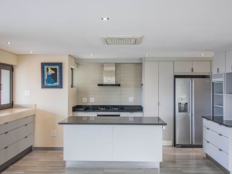 Modern kitchen featuring sleek cabinetry, stone countertops, a central island, and integrated stainless steel appliances with recessed lighting.