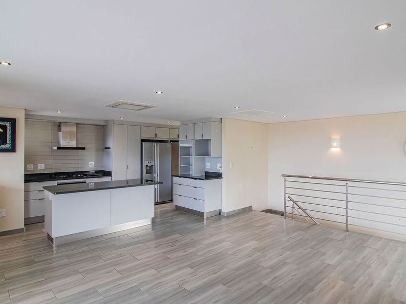 Spacious open-plan kitchen and living area featuring modern cabinetry, a central island, gas hob, and sleek tiled flooring with a stainless steel staircase balustrade.