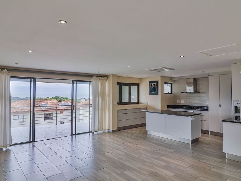 Spacious open-plan living and kitchen area featuring modern cabinetry, a central island, and large sliding doors opening to a balcony with coastal views.