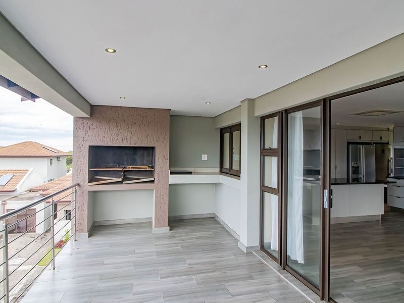 Spacious covered balcony featuring a built-in braai, modern tiled flooring, and seamless access to the interior living area through large sliding glass doors.