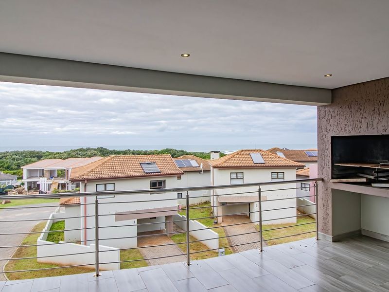 Covered balcony featuring a built-in braai, stainless steel balustrade, and tiled flooring, offering elevated views of the surrounding estate and coastline.