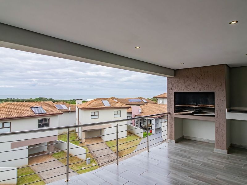 A spacious covered balcony featuring a built-in braai, modern tiled flooring, and a stainless steel balustrade, offering elevated views of the surrounding estate.