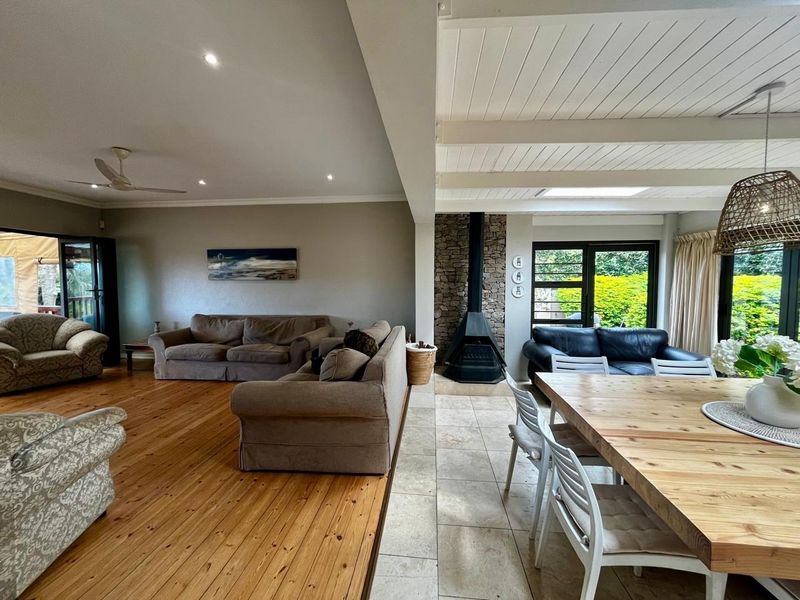 Spacious open-plan living and dining area featuring a mix of timber and stone flooring, a stone-clad fireplace, and a bright, exposed beam ceiling.