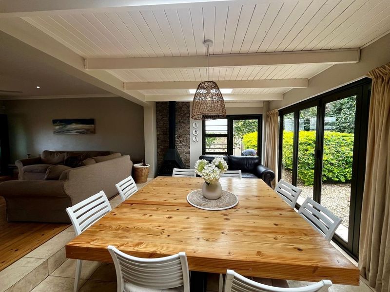Spacious open-plan dining and living area featuring a stone fireplace, exposed beam ceiling, and large sliding doors opening to the garden.
