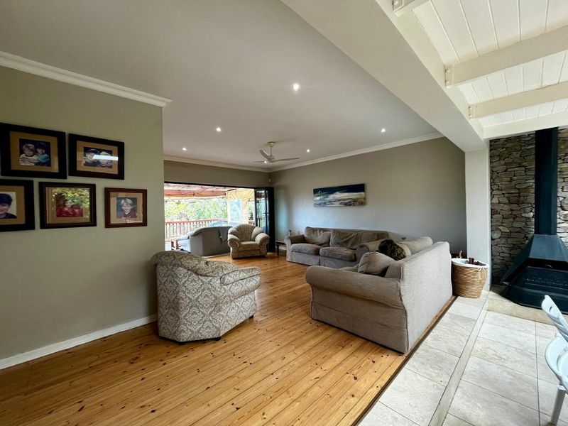 Spacious living room featuring polished hardwood floors, a striking stone fireplace, and bi-fold doors opening to an outdoor deck area.