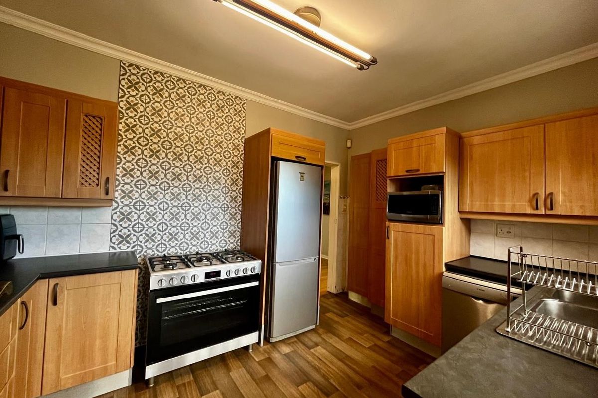 A functional kitchen featuring wooden cabinetry, a gas stove with decorative splashback, built-in microwave, and laminate flooring.