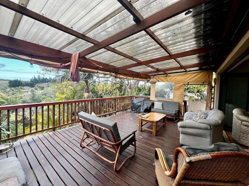 Covered outdoor patio featuring timber decking, a timber pergola structure with a corrugated roof, and a balustrade overlooking the surrounding landscape.