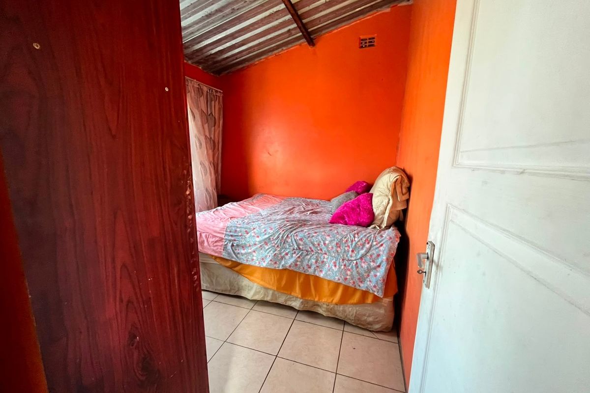 A bedroom featuring tiled flooring and an exposed corrugated metal ceiling, requiring cosmetic updates to improve the overall finish and aesthetic appeal.