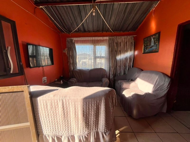 A living room featuring tiled flooring, an aluminium window, and an exposed corrugated metal ceiling with vibrant orange wall finishes.