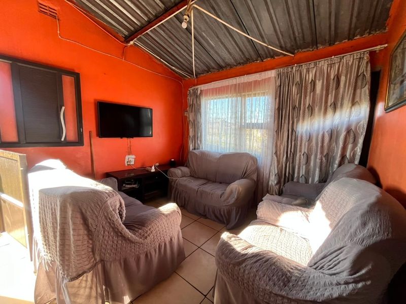 A living room featuring tiled flooring and an exposed corrugated metal ceiling, requiring cosmetic updates to improve the overall finish and aesthetic appeal.