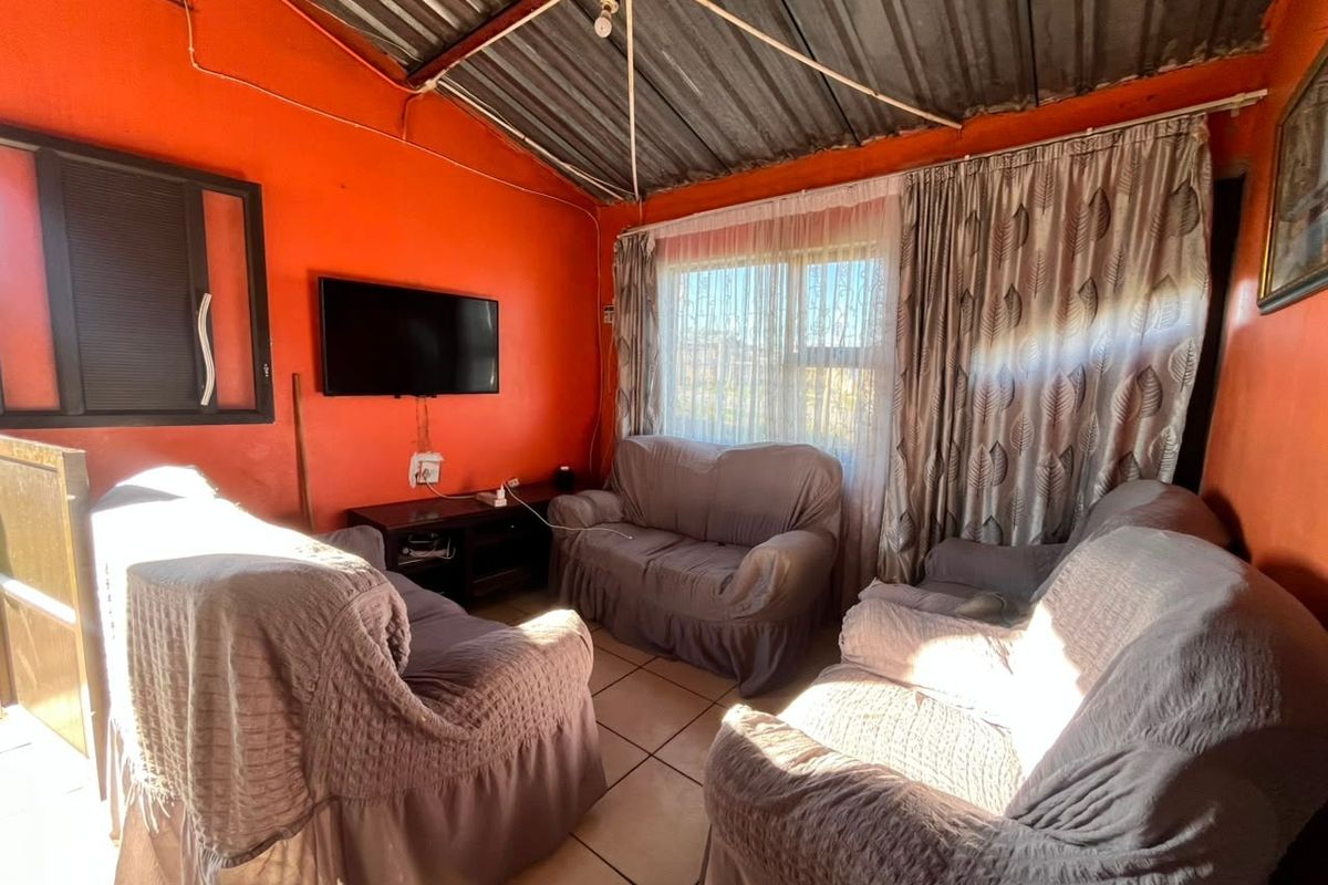 A living room featuring tiled flooring and an exposed corrugated metal ceiling, requiring cosmetic updates to improve the overall finish and aesthetic appeal.