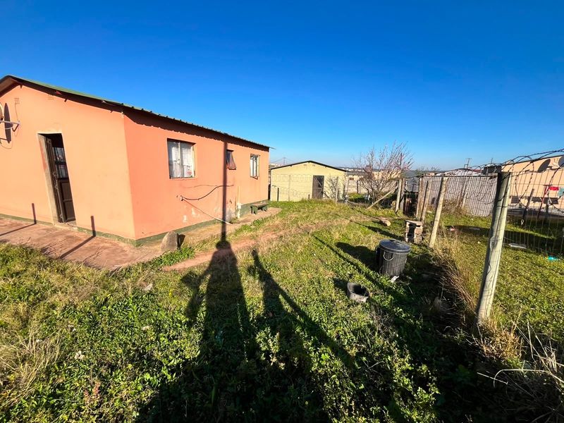 Rear view of the property showing the exterior wall, corrugated roof, and surrounding yard area enclosed by wire fencing.