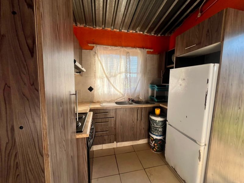 Compact kitchen featuring wood-look cabinetry, laminate countertops, built-in hob, extractor fan, and tiled flooring with an exposed corrugated metal ceiling.