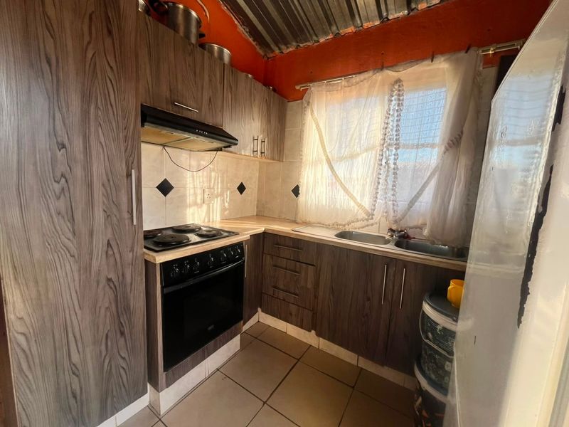 Compact kitchen featuring wood-look cabinetry, built-in electric stove with extractor, and tiled backsplash. Requires ceiling and wall finishing to improve aesthetic appeal.