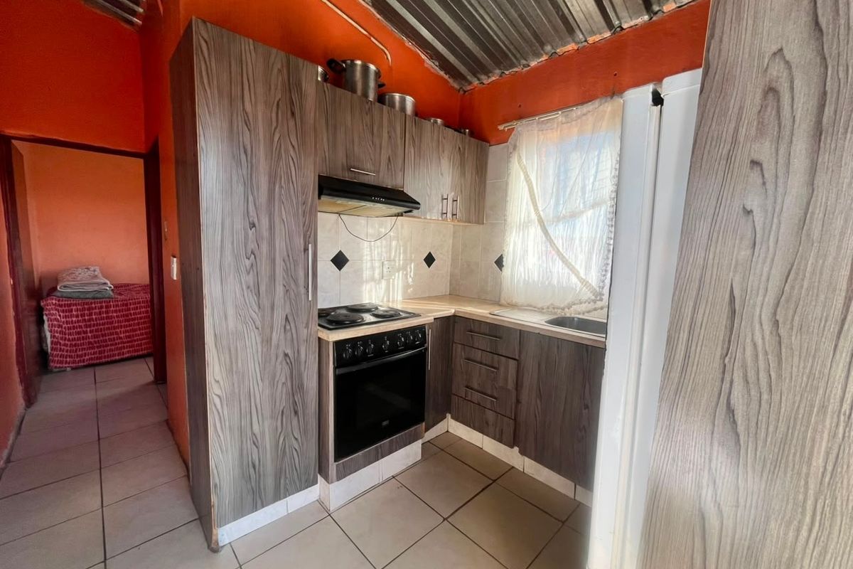 Compact kitchen featuring wood-look cabinetry, electric stove with extractor, tiled flooring, and an exposed corrugated metal ceiling.