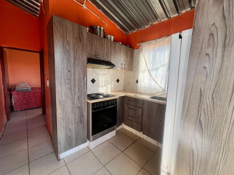 Compact kitchen featuring wood-look cabinetry, electric stove with extractor, tiled flooring, and an exposed corrugated metal ceiling.