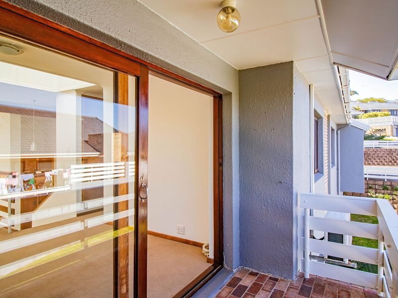 A covered balcony featuring brick flooring, a white railing, and a sliding glass door providing access to the interior living space.