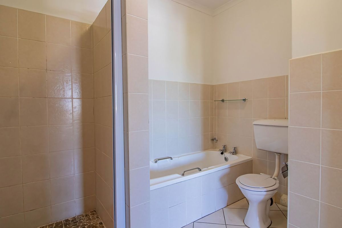 A functional bathroom featuring a separate shower enclosure, a bathtub, and a toilet with neutral wall and floor tiling.